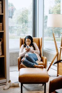 woman sitting in a brown leather chair smelling a scented soy candle